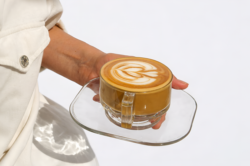 Koatji latte with delicate foam art served in clear glassware on a minimalist saucer.