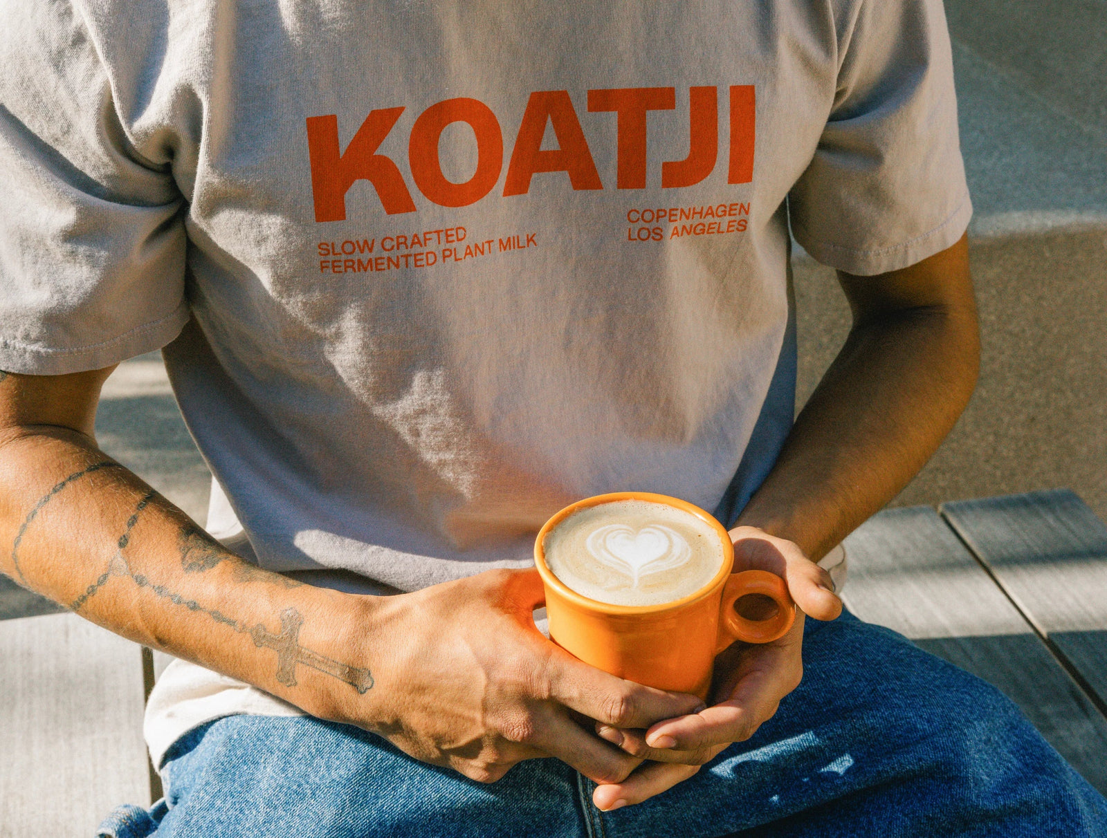 Person holding a latte wearing a Koatji slow-crafted fermented plant milk t-shirt.