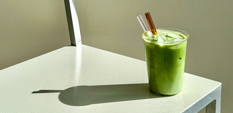 Iced green matcha latte made with Koatji, sitting on a sunlit white chair with long shadows.