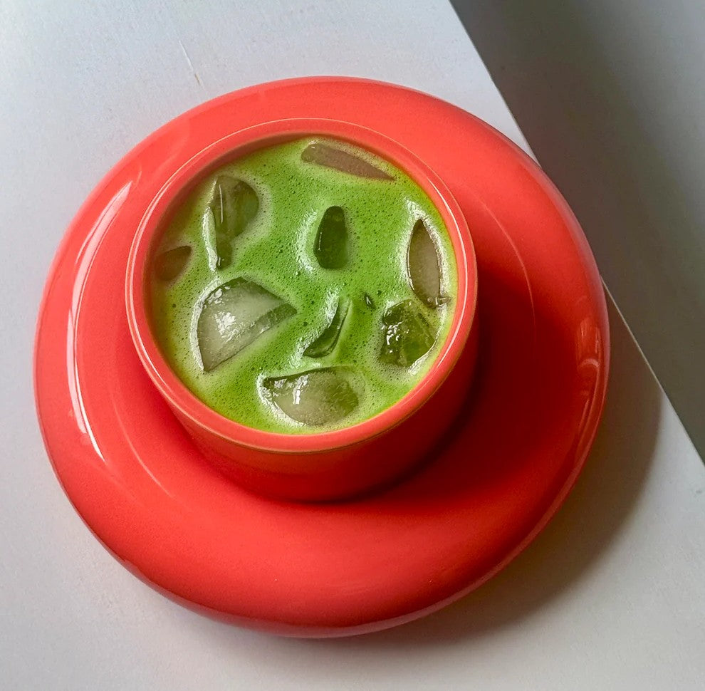 Iced matcha in a coral cup and saucer made with Koatji, sitting on a sunlit surface.