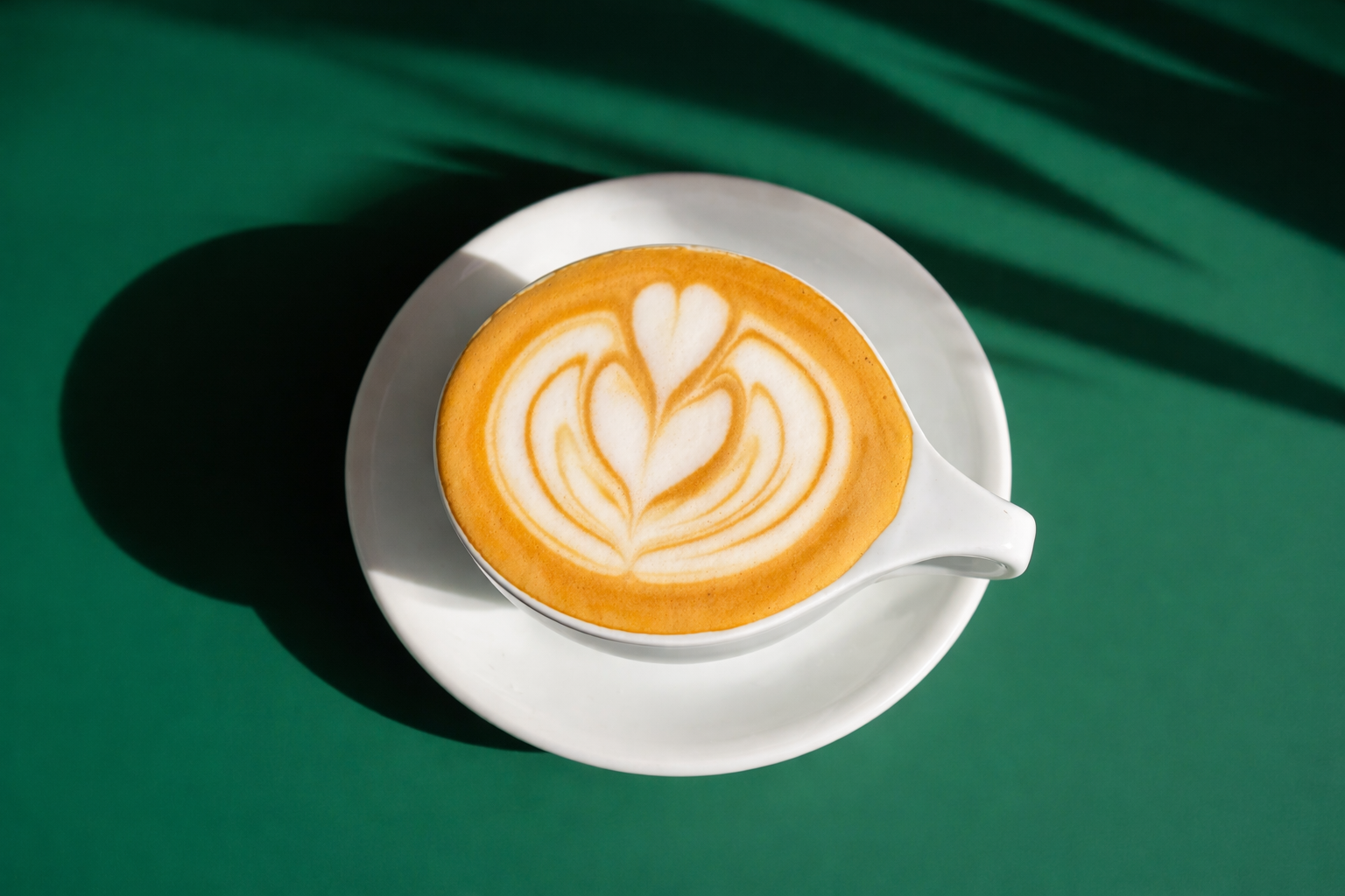 Latte with leaf latte art made using Koatji, served in a clear glass cup on a green background. 
