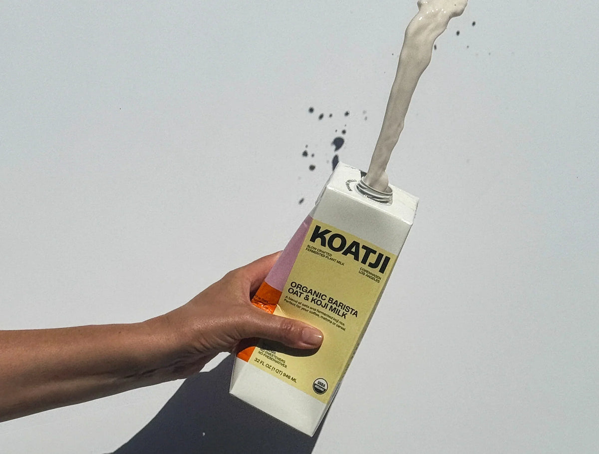 Organic Barista Oat & Koji milk pouring out of a KOATJI carton held in hand.