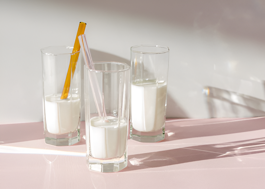 Three glasses of KOATJI oat & koji milk on a pink surface with reusable straws.